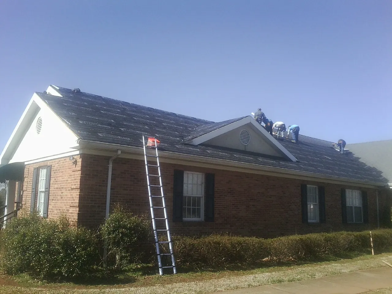 Crew tearing shingles off a brick ranch roof with a ladder set — Metal Roof Repair work by our crew in Perth Amboy
