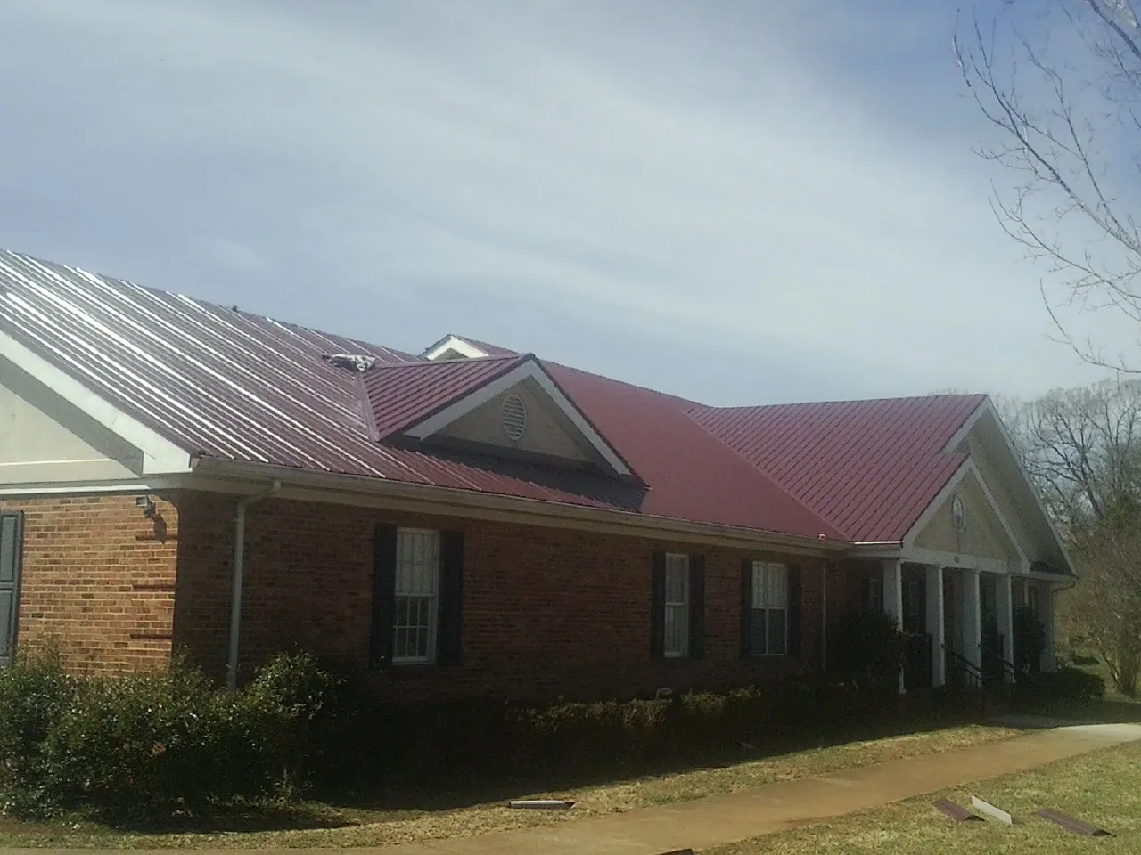 Red metal roof with gabled entries on a long brick building, from a Hail Damage Roof Repair job in Perth Amboy