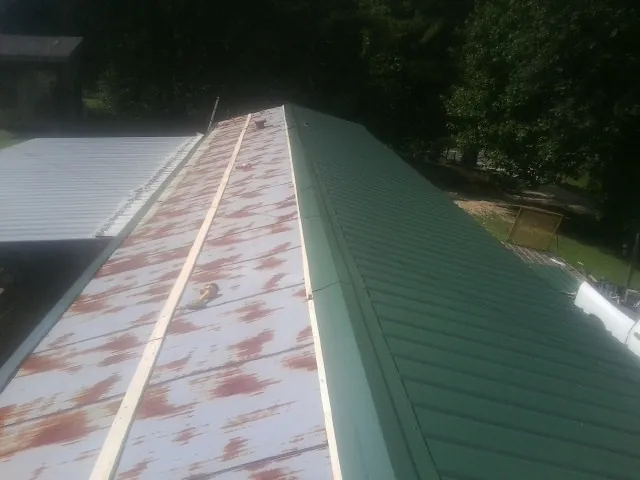 Old rusted panels beside newly installed green metal roofing — Wind Damage Roof Repair by Roofing Brothers in Perth Amboy