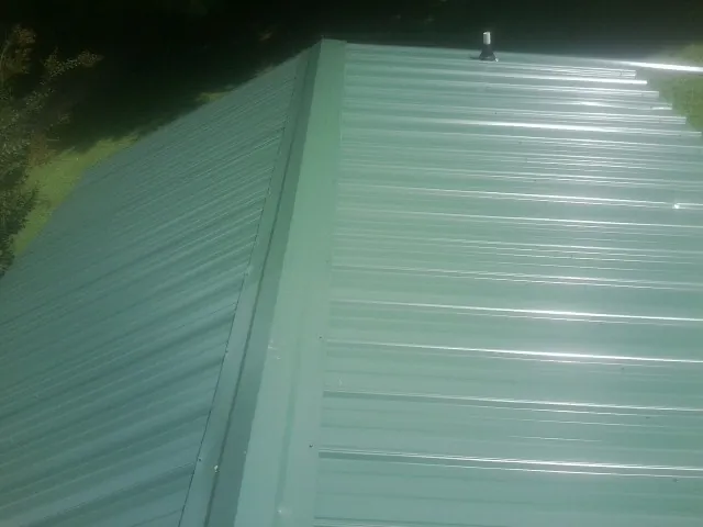 New green metal panels meeting at the ridge of a roof — Flat Roof Repair work by our crew in Perth Amboy