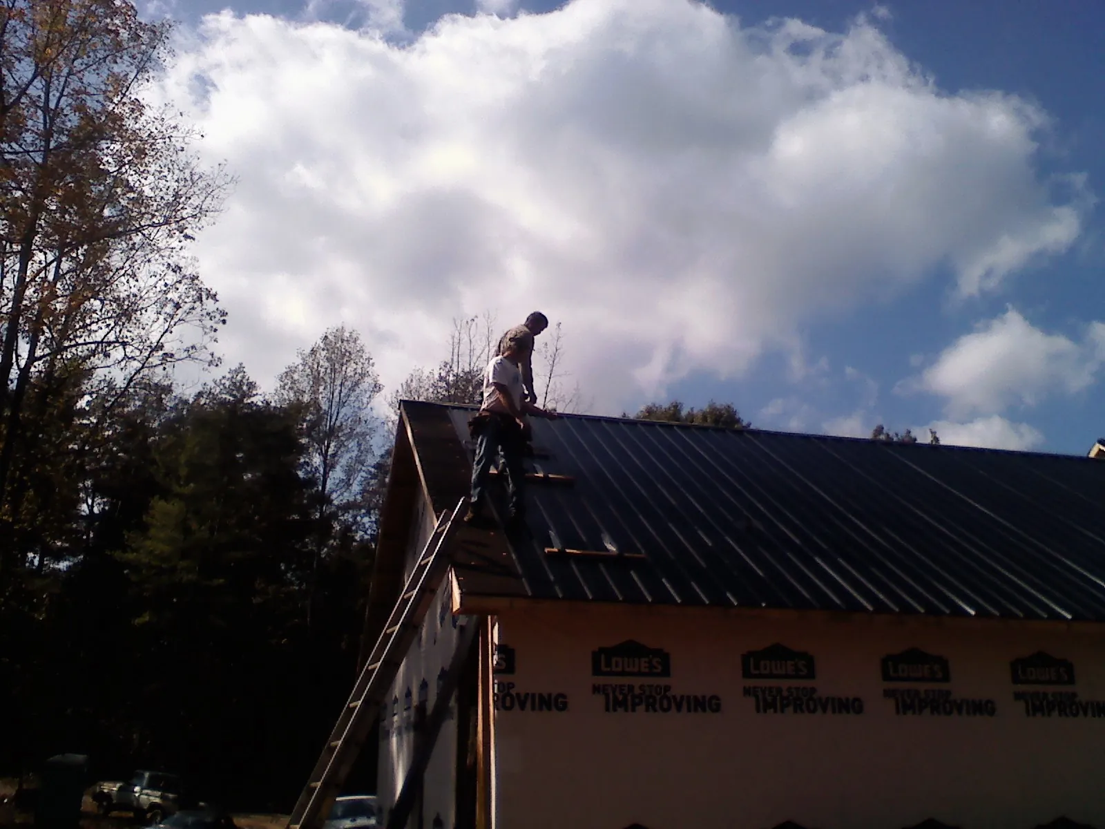Roofer fastening dark metal panels high against a cloudy sky, from a Roof Inspection job in Perth Amboy