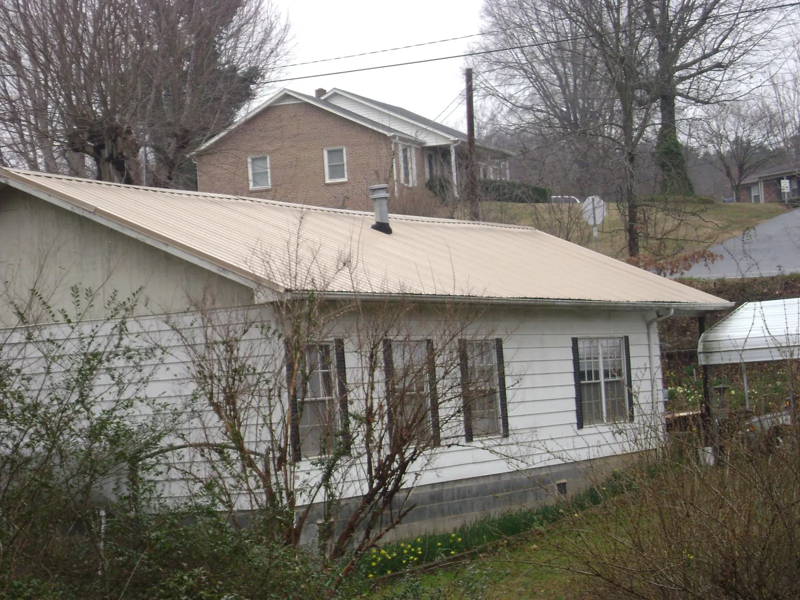 Tan metal roof on a white sided house set into a hillside — Commercial Roofing by Roofing Brothers in Perth Amboy